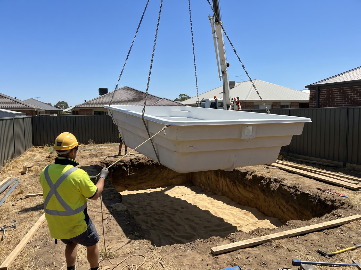 A crane lowering a fibreglass pool shell into a dug hole